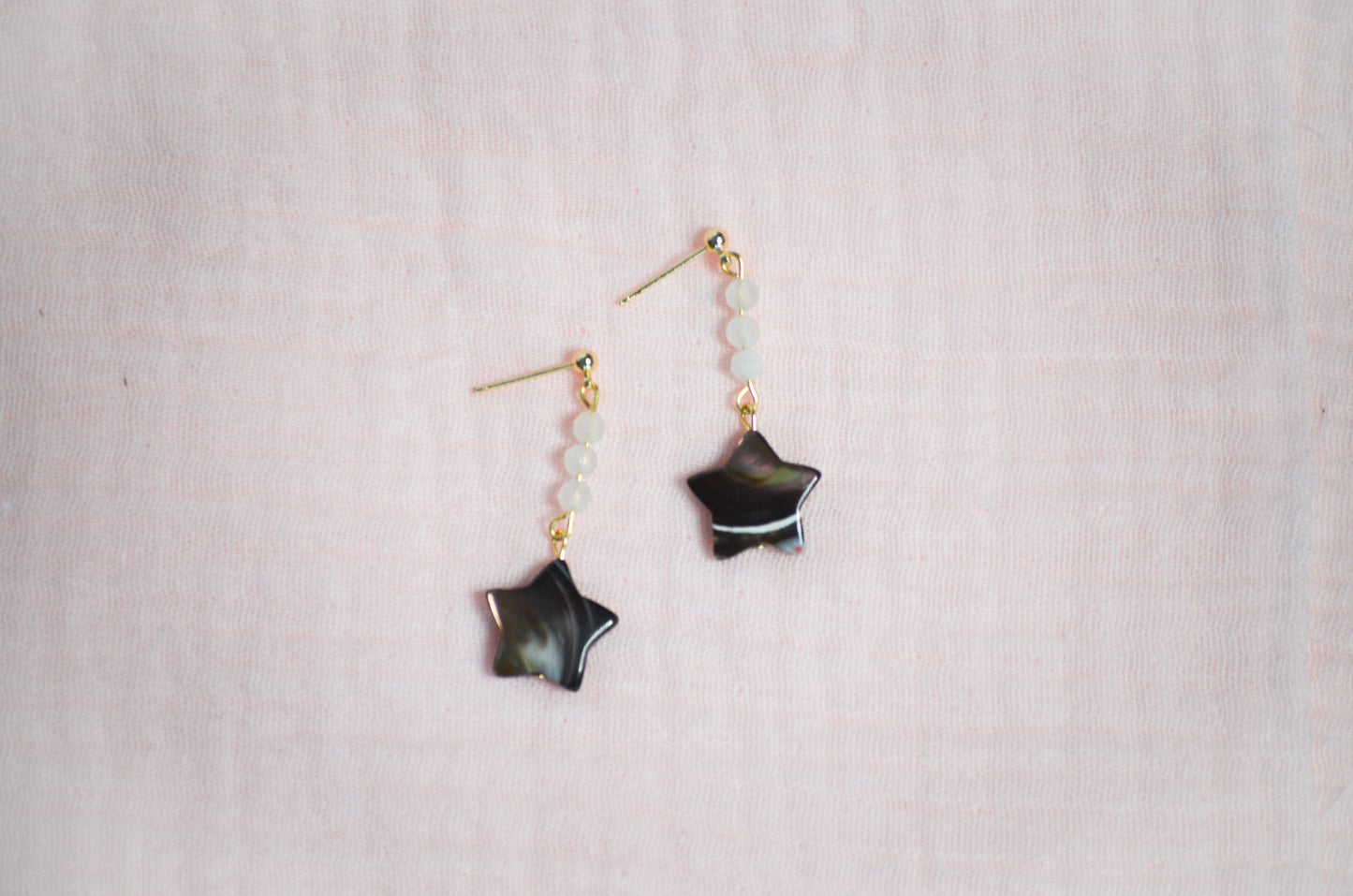 Star-shaped earrings on a light pink fabric background