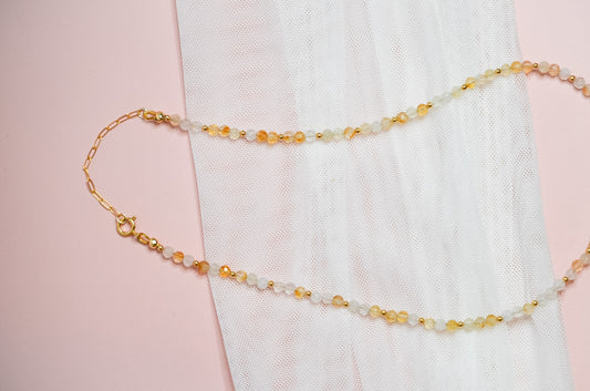 Necklace with yellow, white and gold beads and a gold clasp on a pink background
