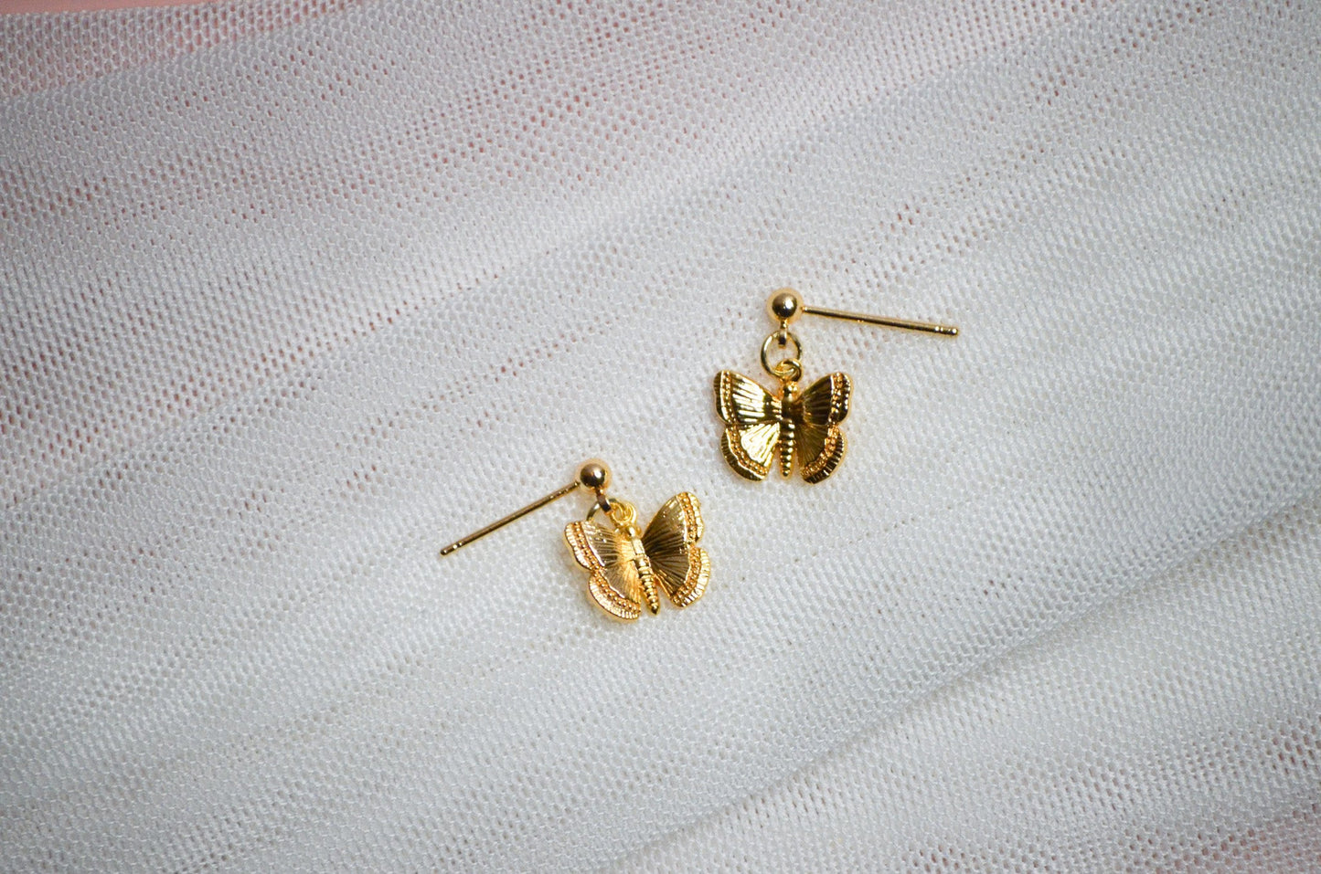 Gold butterfly-shaped stud earrings on a light fabric background