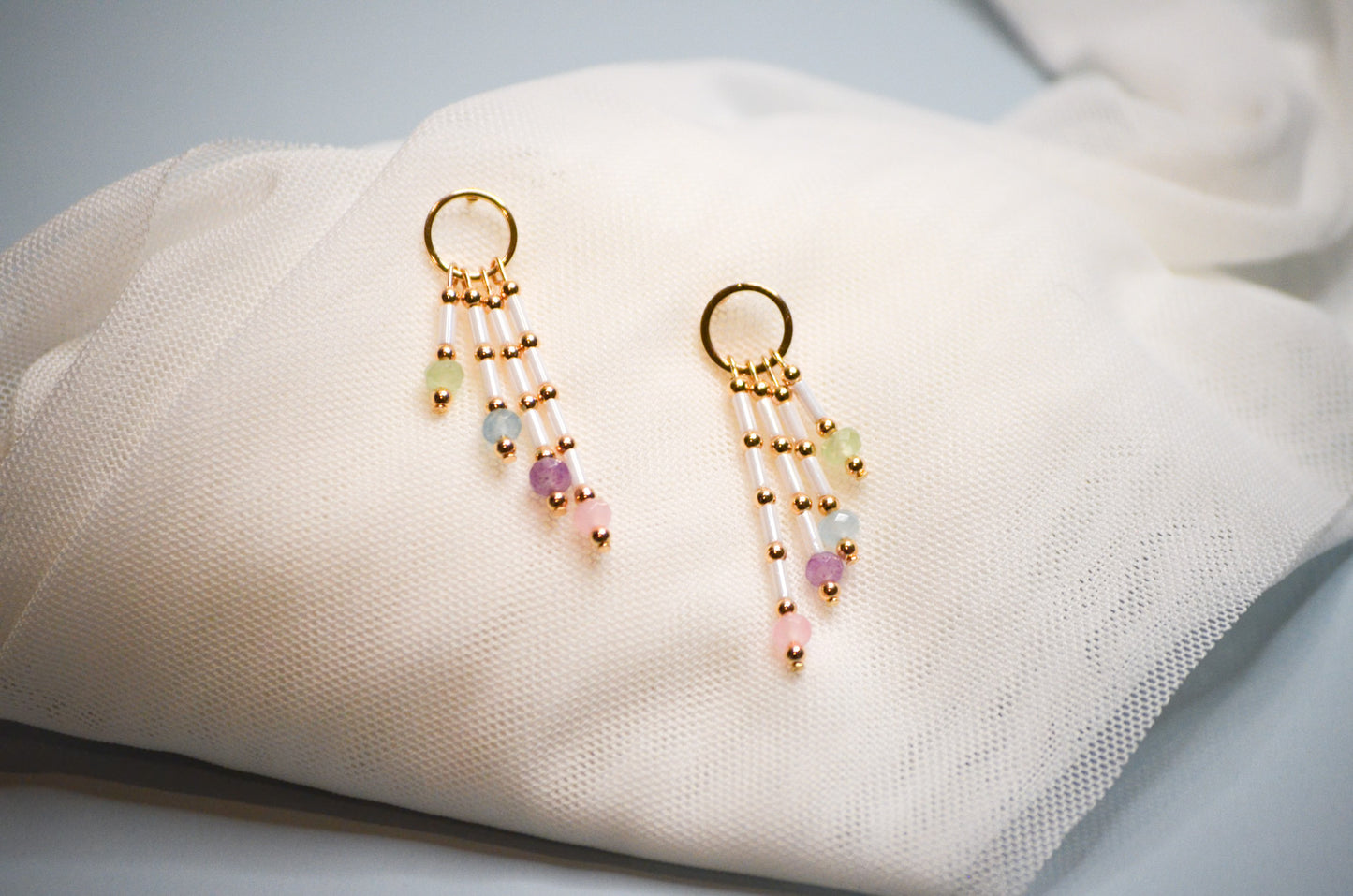 Pair of gold circle earrings with colorful dangle beads on a white fabric background