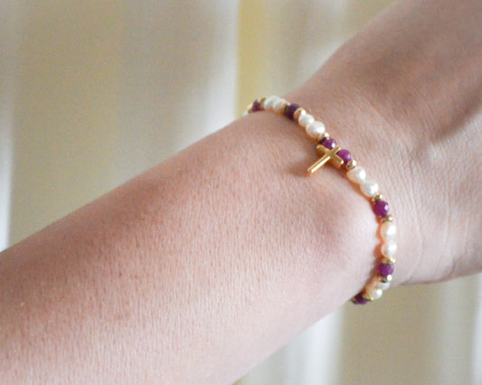 Pearl, gold, and gemstone bracelet with cross charmon a wrist with a neutral background