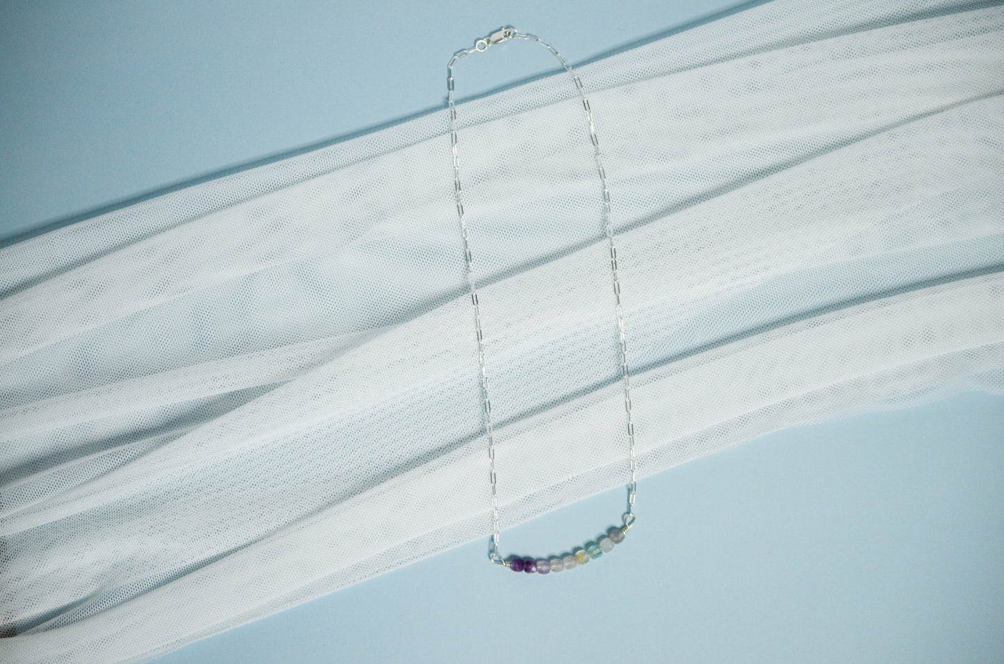 Silver chain necklace with colorful beads on a light blue background