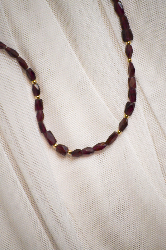 Necklace with burgundy and gold beads on a white fabric background.