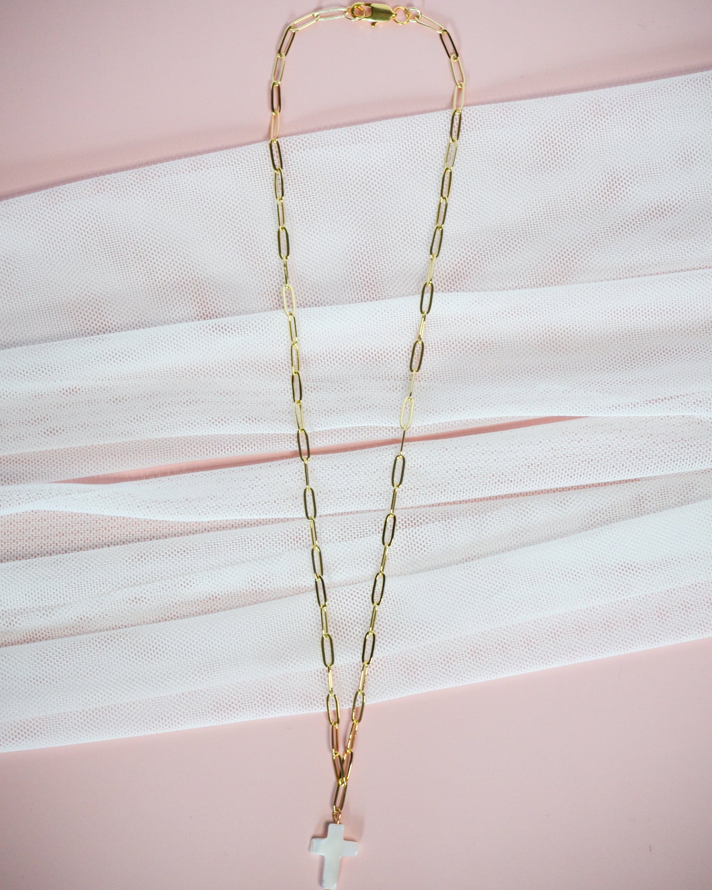 Gold chain necklace with a cross pendant on a pink background