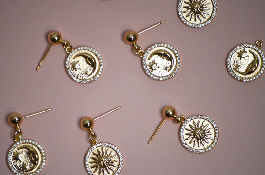 Seven gold dangle earrings with sun and moon designs on a pink background