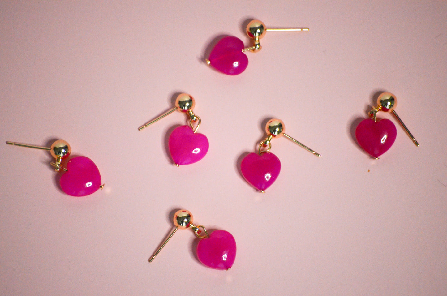 Heart-shaped pink earrings with gold accents on a pink background