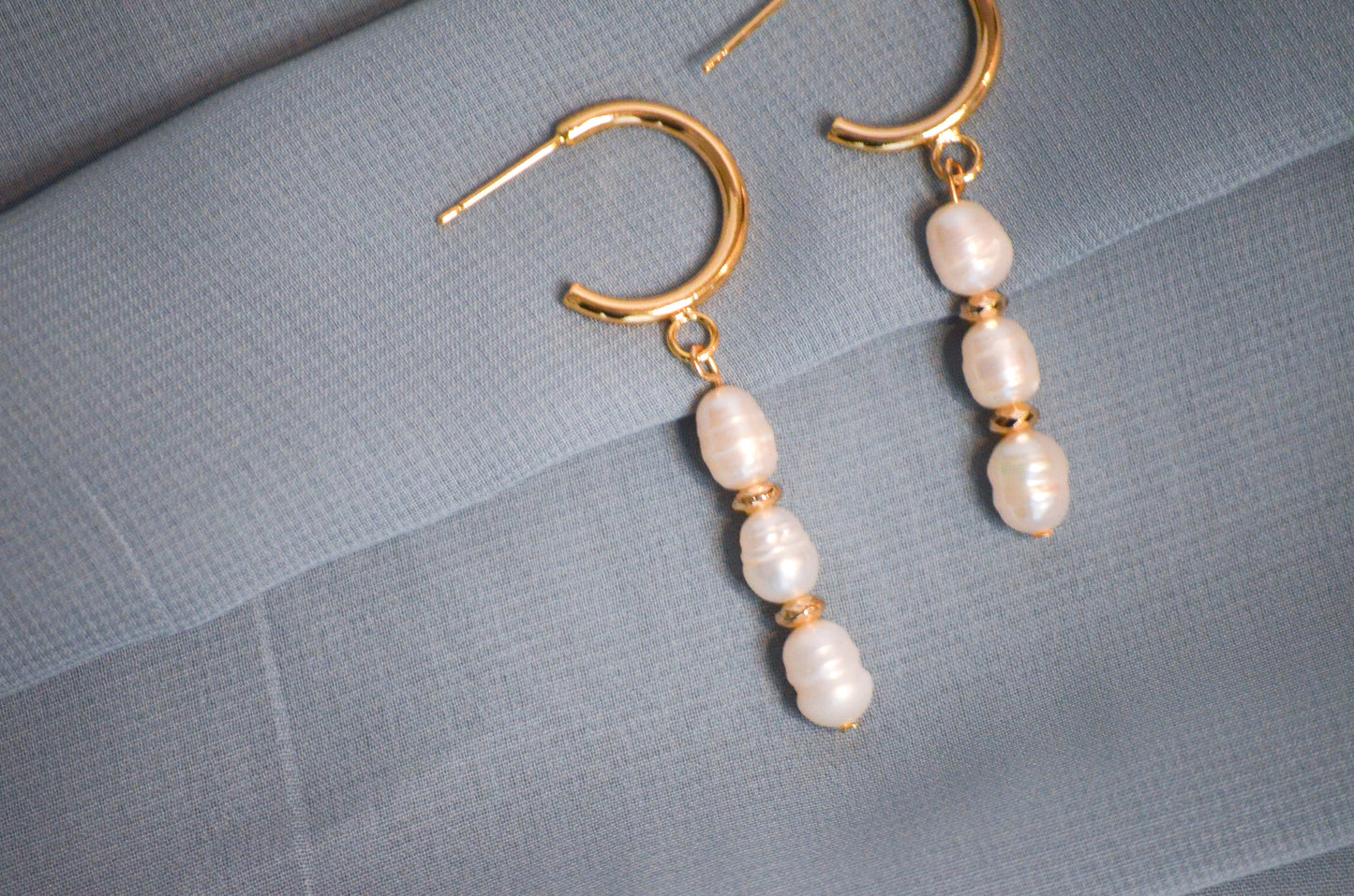 Pearl earrings with gold hooks on a gray textured surface