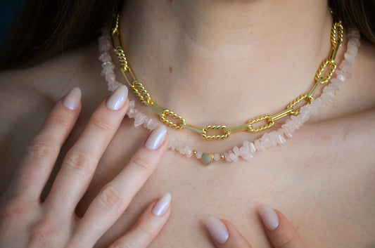 Gold chain necklace with pink stones and gold heart beads worn by a woman with light pink nails