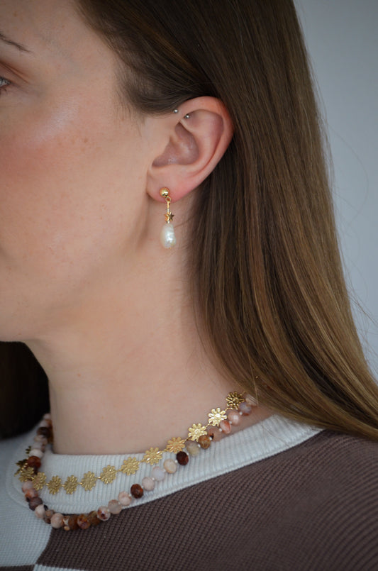 Close-up of a person wearing pearl earrings, a gold chain necklace, and a beaded necklace.
