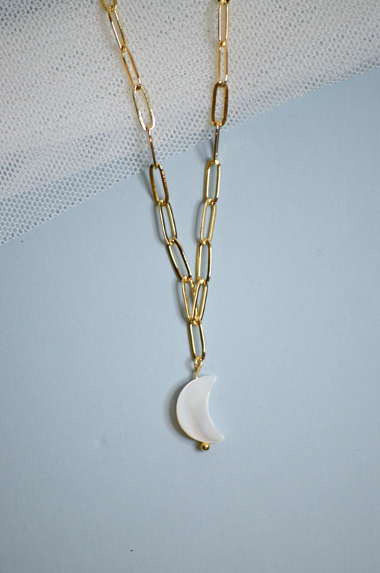 Gold chain necklace with a white mother of pearl crescent moon pendant on a light blue background