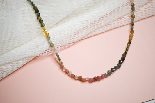 Multicolored green, pink, and yellow beaded necklace on a pink and white fabric background