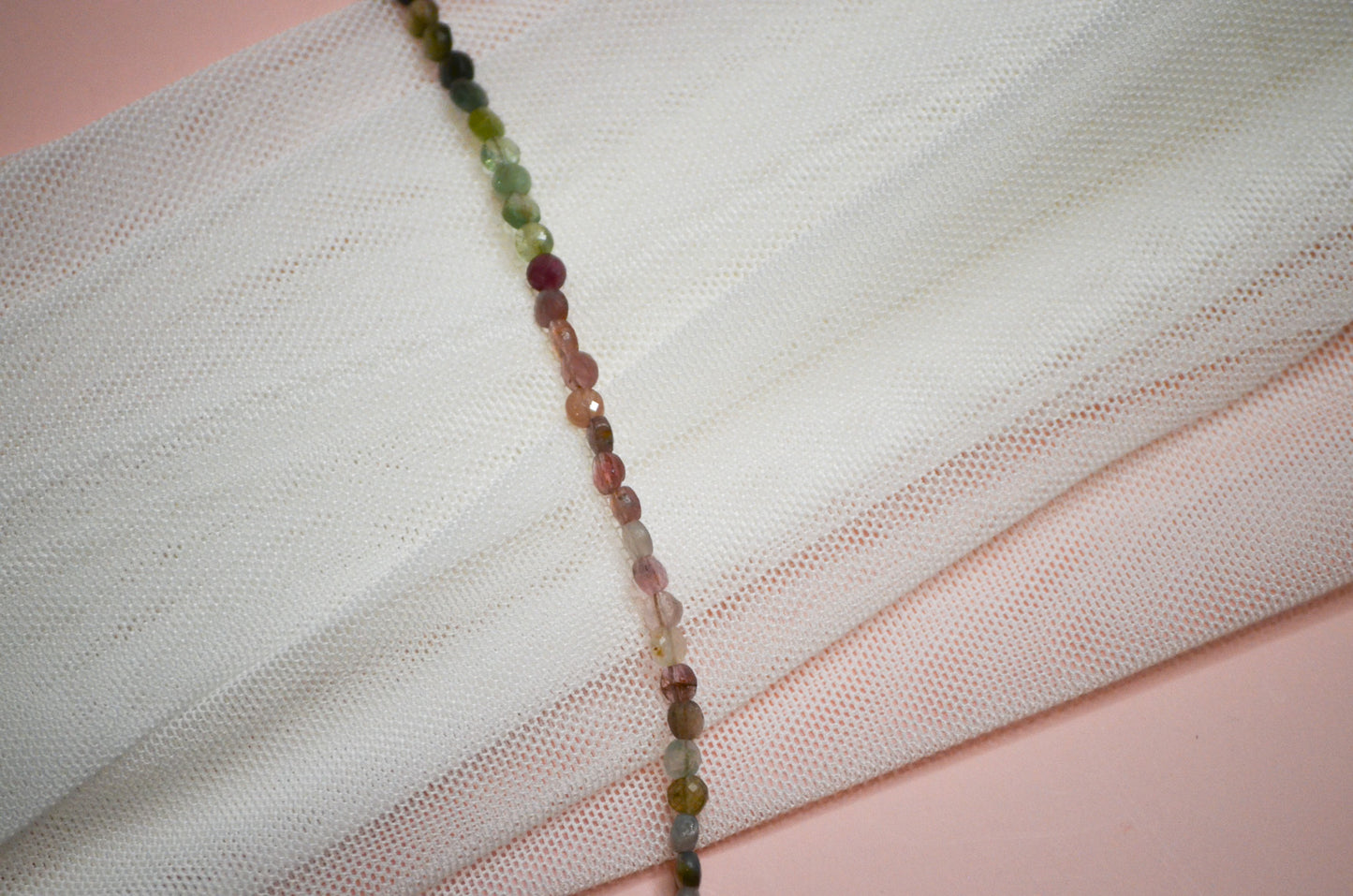 Multicolored green and pink beaded necklace on a white fabric background