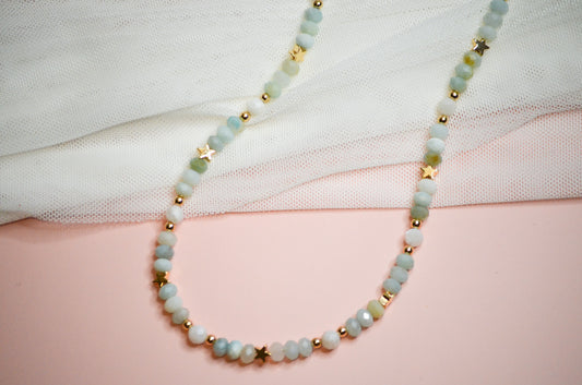 Necklace with light blue beads and gold star accents on a white and pink background