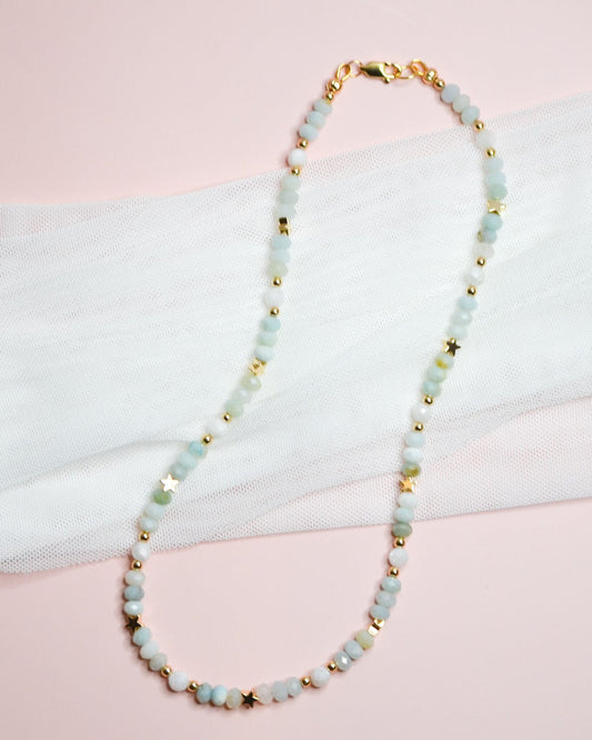 Necklace with light blue beads and gold star accents on a white and pink fabric background