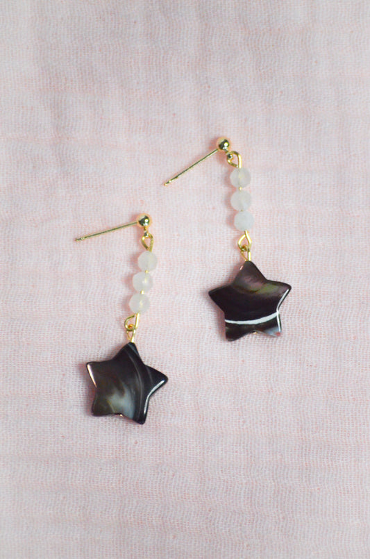 Star-shaped earrings with gold accents on a light pink background