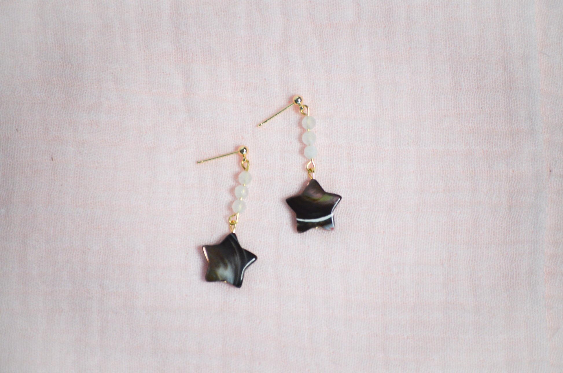 Star-shaped earrings on a light pink fabric background