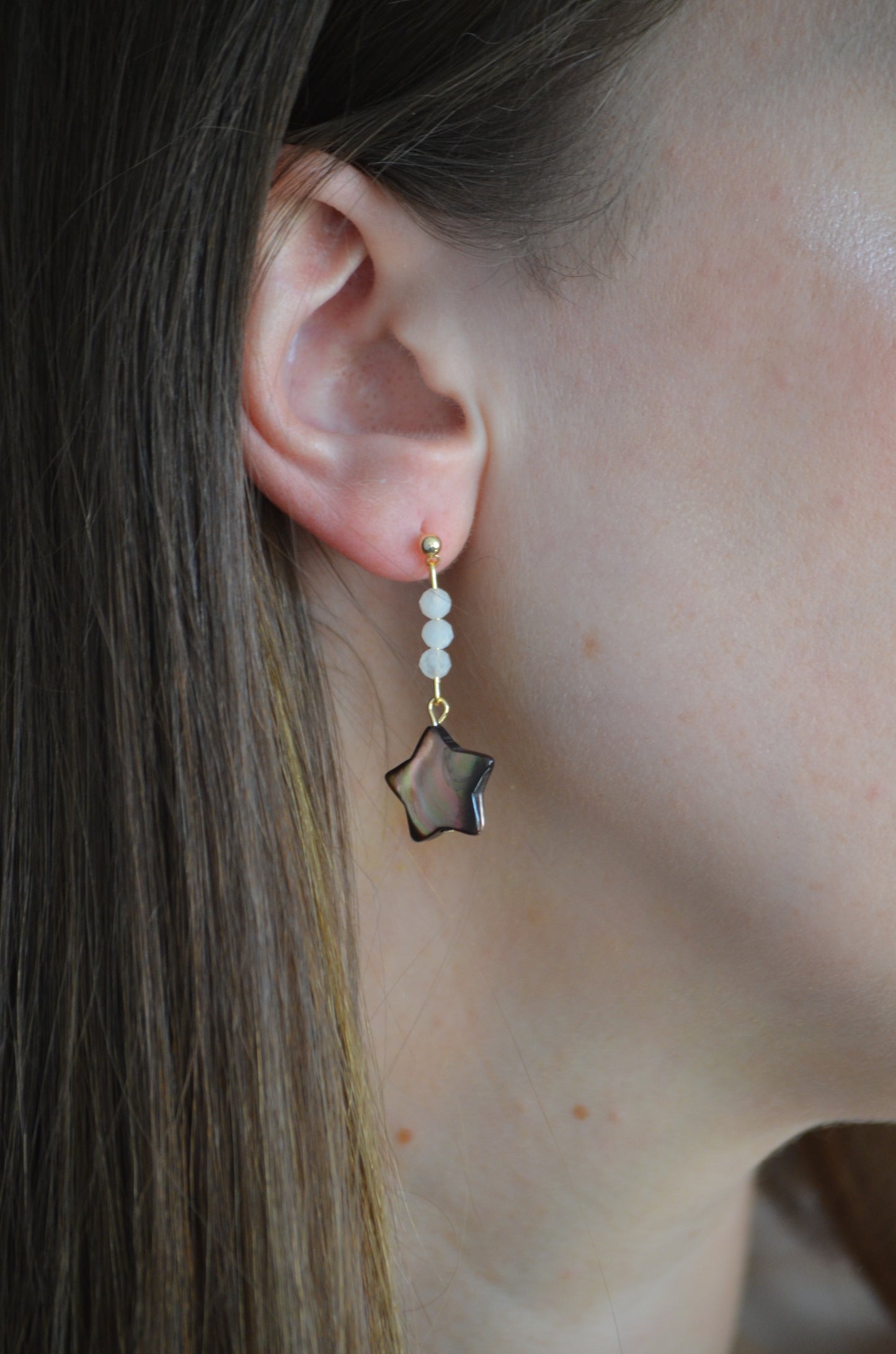 Close-up of an ear wearing a dangle star-shaped earring with beads.