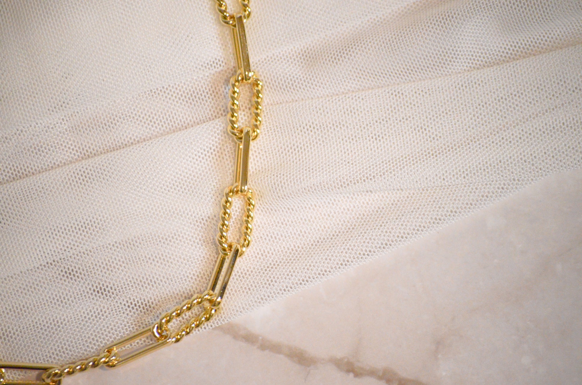 Textured gold chain necklace on a textured white surface