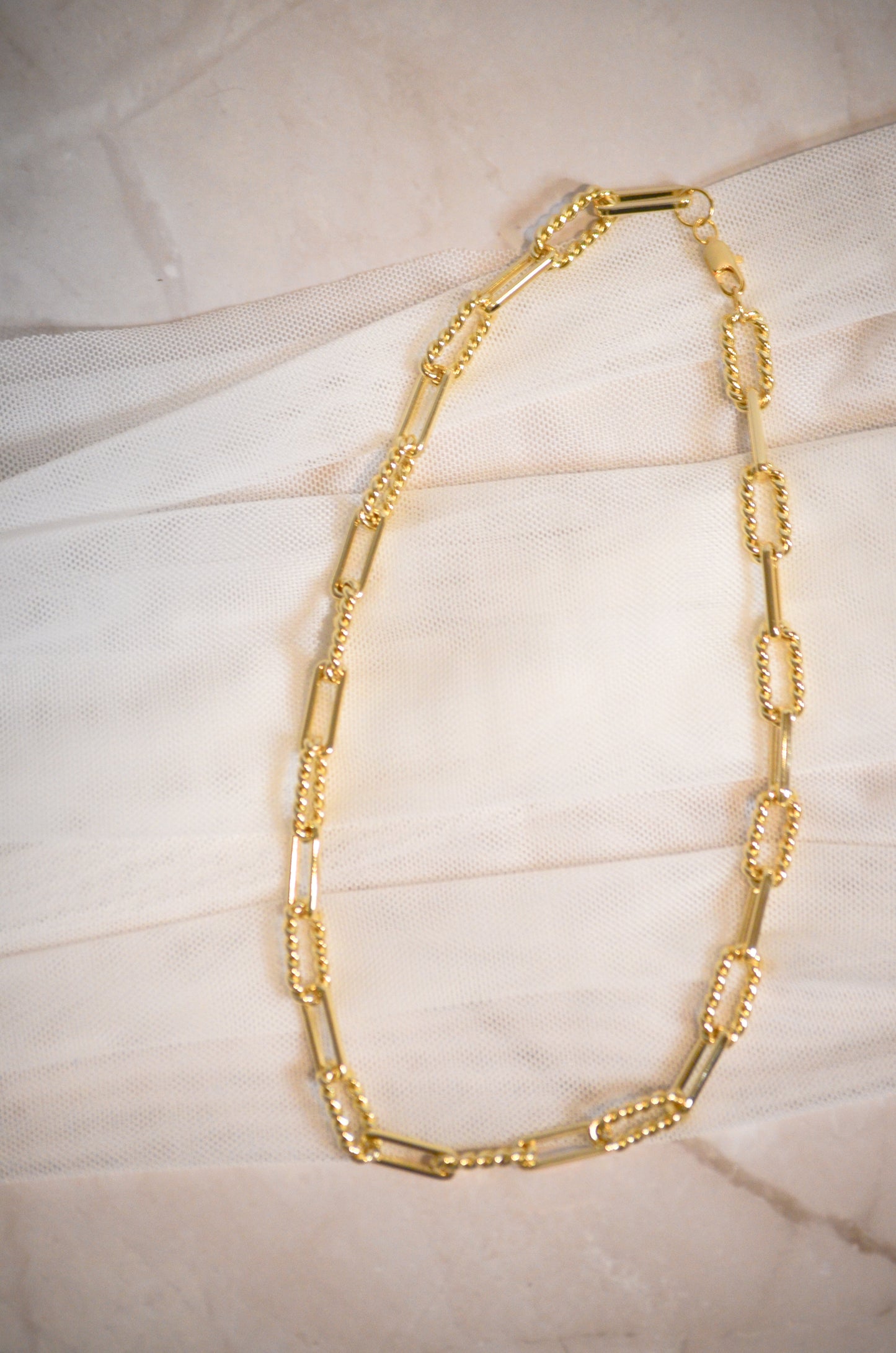 Gold chain necklace on a textured beige surface