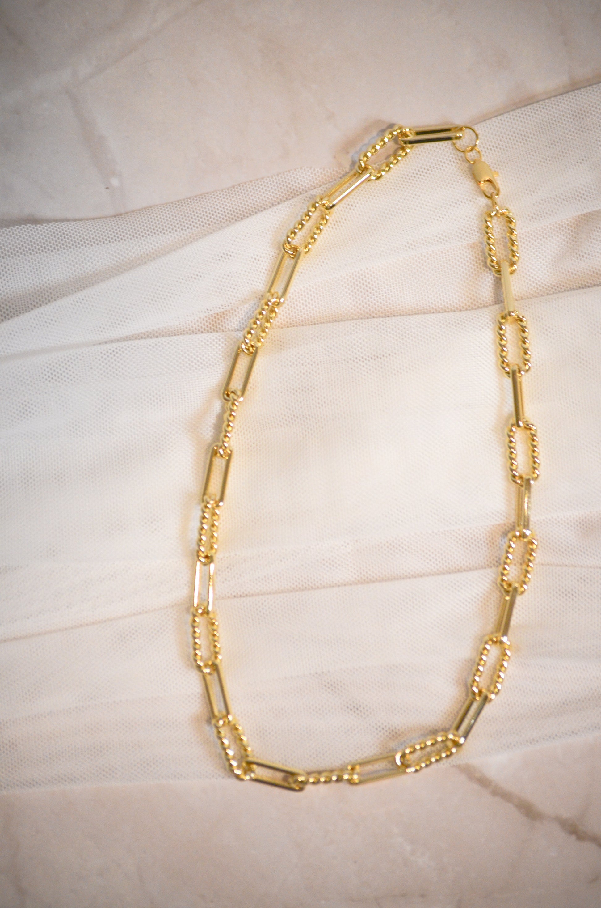 Gold chain necklace on a textured beige surface