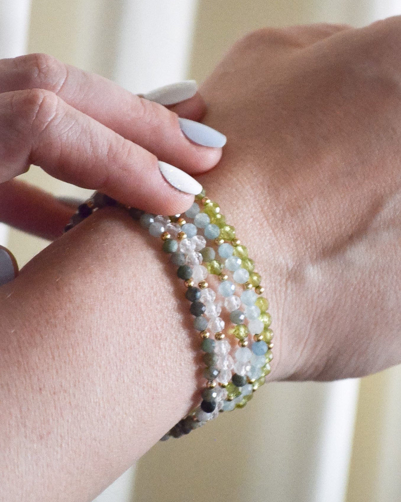 Close-up of a hand wearing a set of beaded bracelets with a blurred background