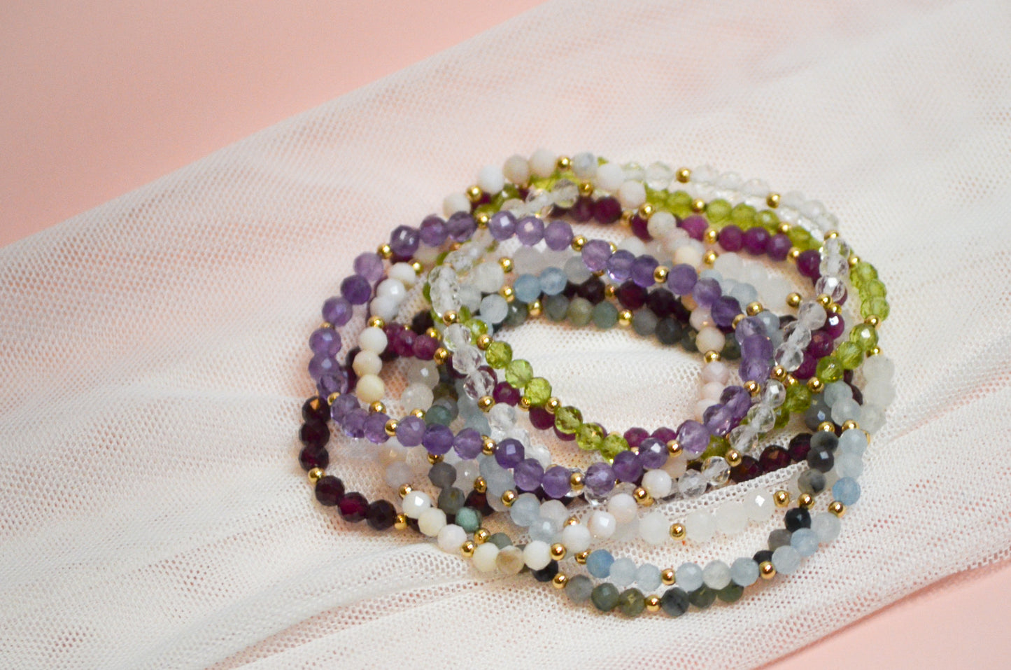 Stack of multicolored beaded bracelets on a light pink fabric background