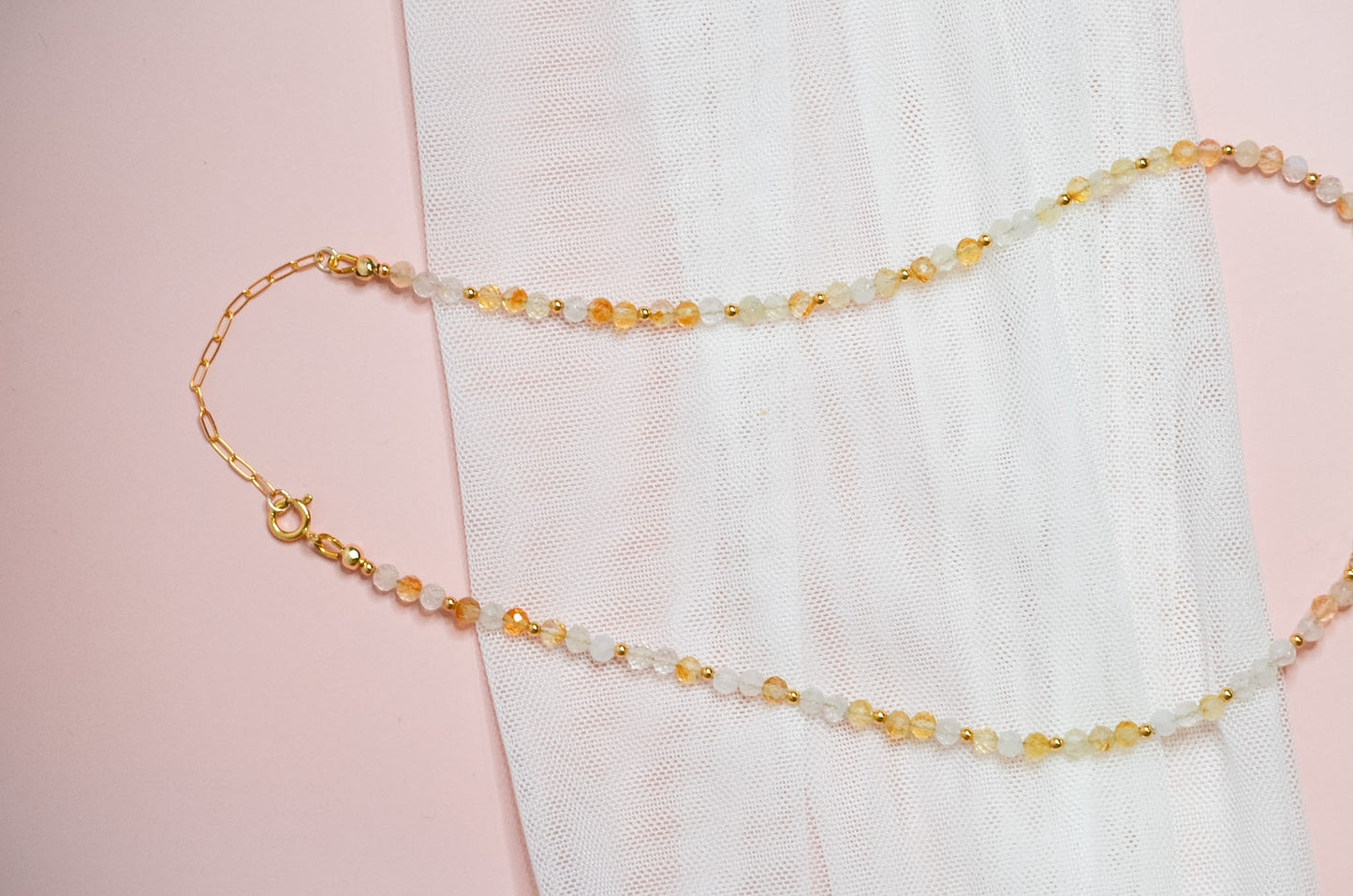 Necklace with yellow, white and gold beads and a gold clasp on a pink background