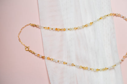 Necklace with yellow, white and gold beads and a gold clasp on a pink background