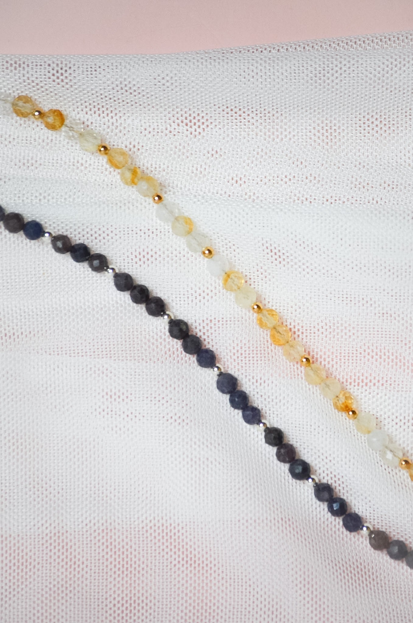 Two beaded necklaces with either gold or silver beads on a textured white surface