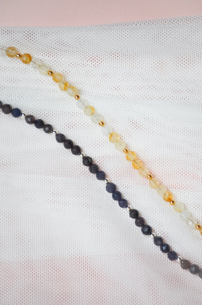 Two beaded necklaces with either gold or silver beads on a textured white surface