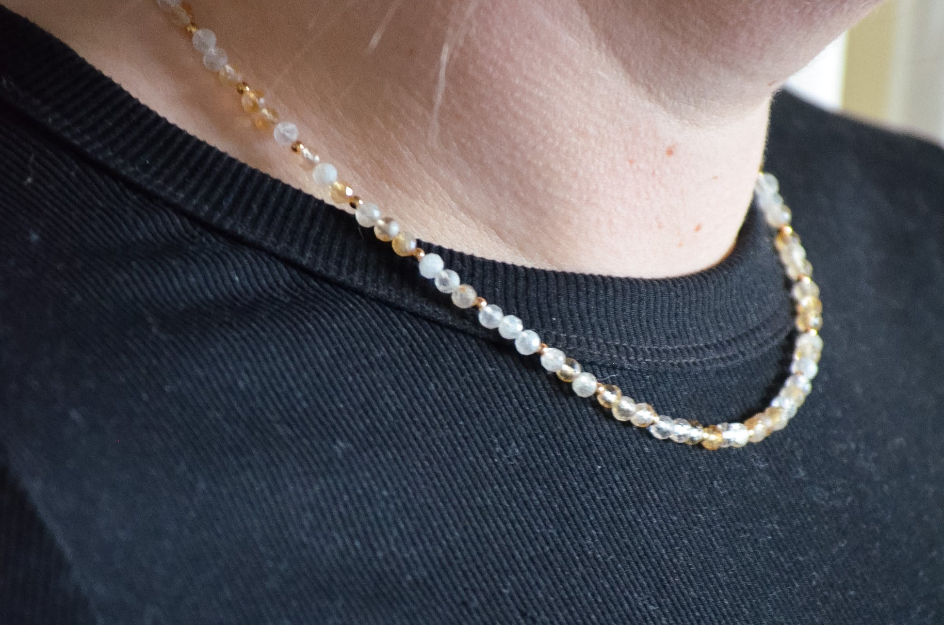 Close-up of a person wearing a delicate beaded necklace on a plain background