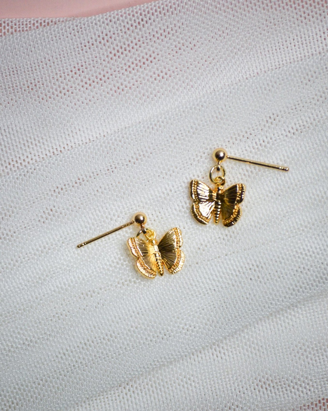 Gold butterfly-shaped stud earrings on a textured white surface