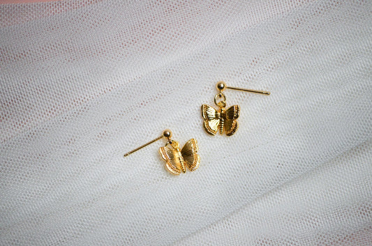 Gold butterfly-shaped stud earrings on a light fabric background