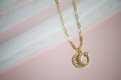 Gold necklace with a gold sun and star pendant on a pink surface.