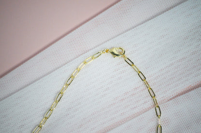 Gold necklace with a lobster shaped clasp on a textured fabric surface with a pink background.