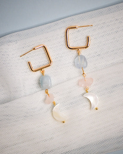 Pair ofgold dangle  earrings with gold frames and multicolored beads circular and moon shaped on a textured fabric background