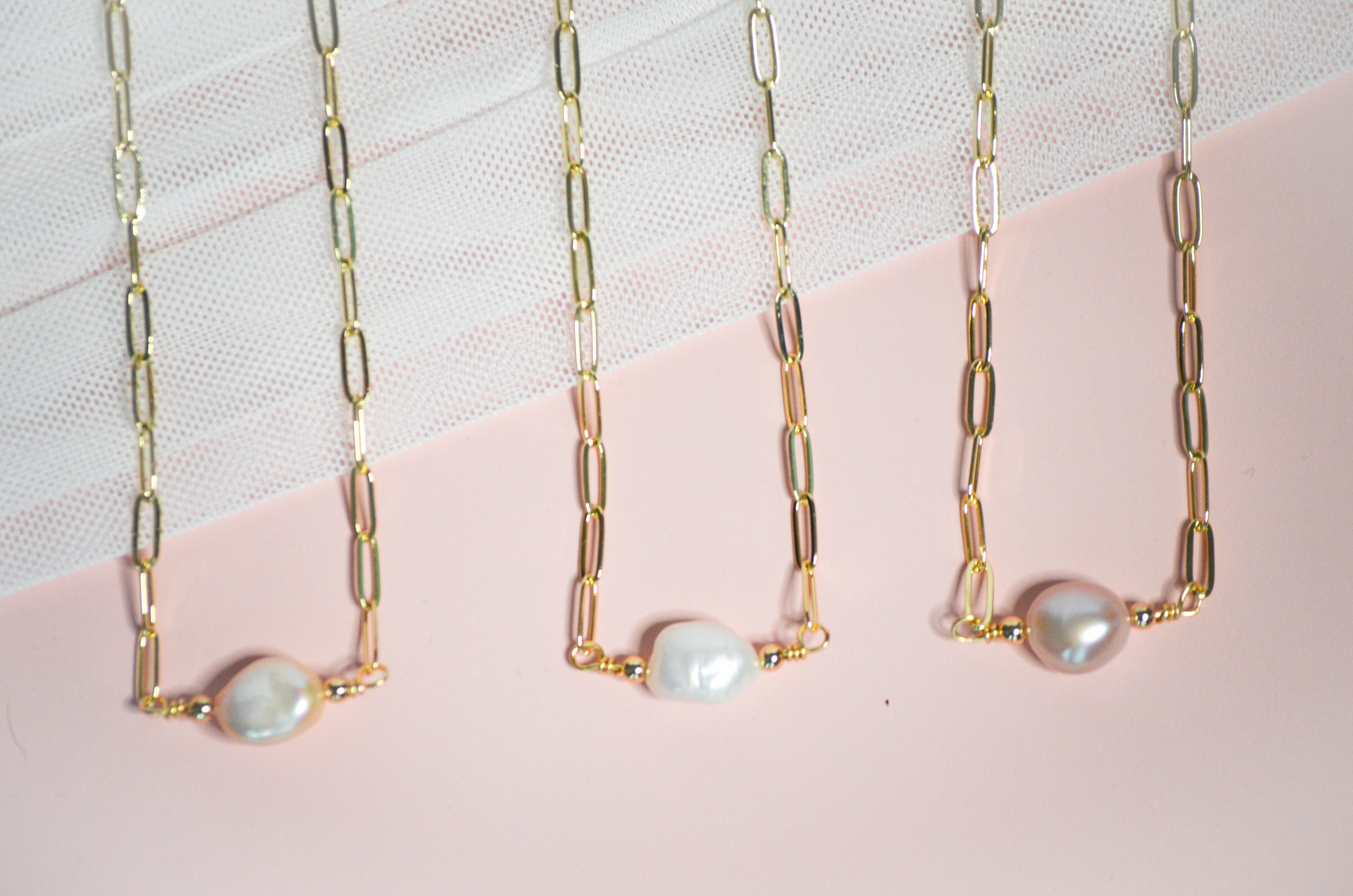 Three pearl necklaces with vafrying shades on a gold chain and pink background