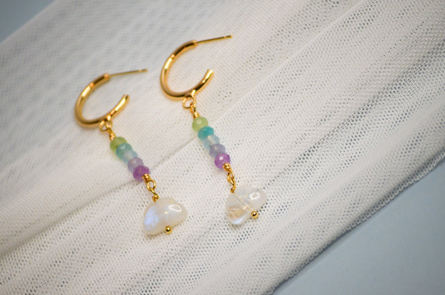 Pair of gold hoop dangle earrings with colorful beads and cloud shaped beads on a textured fabric background