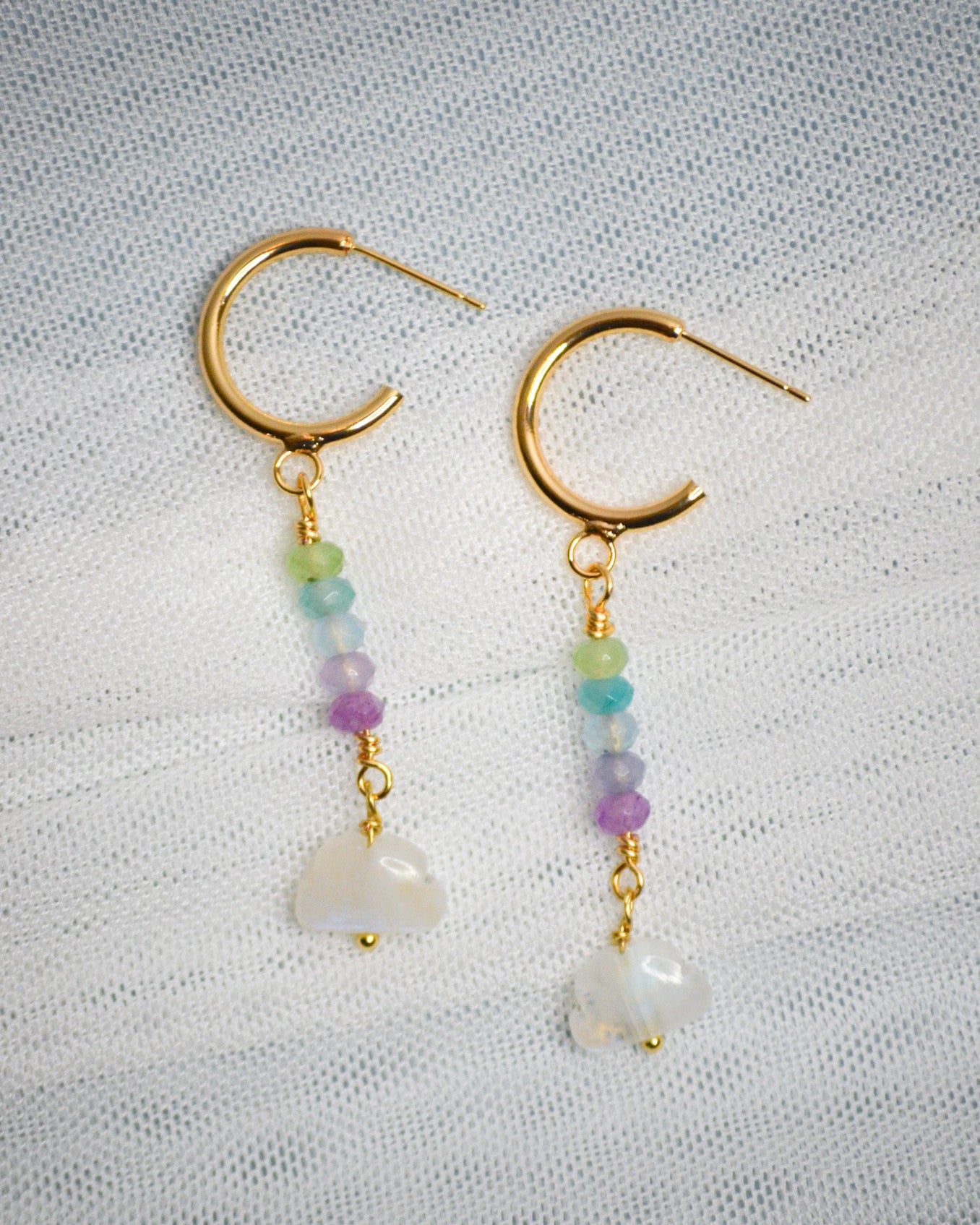 Pair of gold hoop earrings with colorful and cloud shape beads on a textured light blue and white background.
