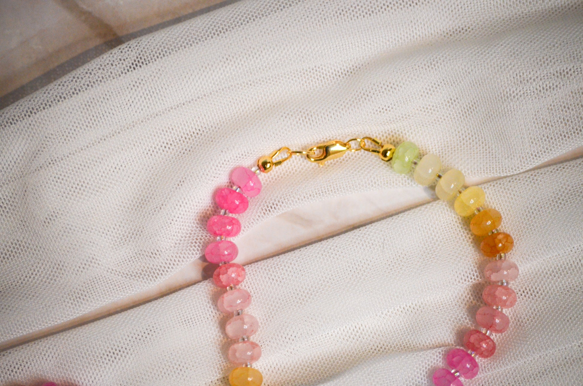 Colorful beaded bracelet with a gold clasp on a white fabric background