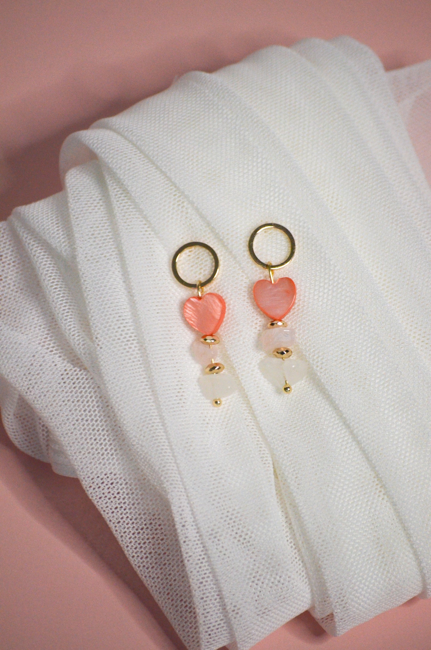 Pair of earrings with pink heart-shaped charms, gold, and clear on a white fabric background