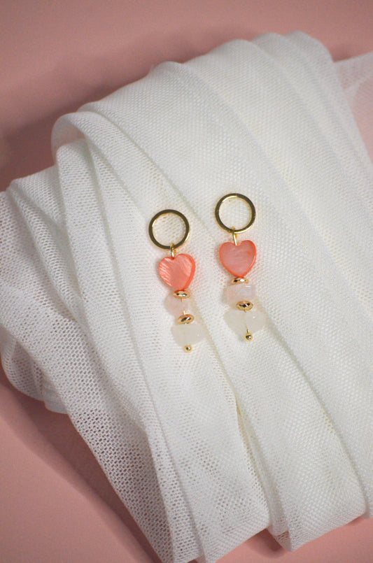 Pair of earrings with pink heart-shaped charms, gold, and clear on a white fabric background