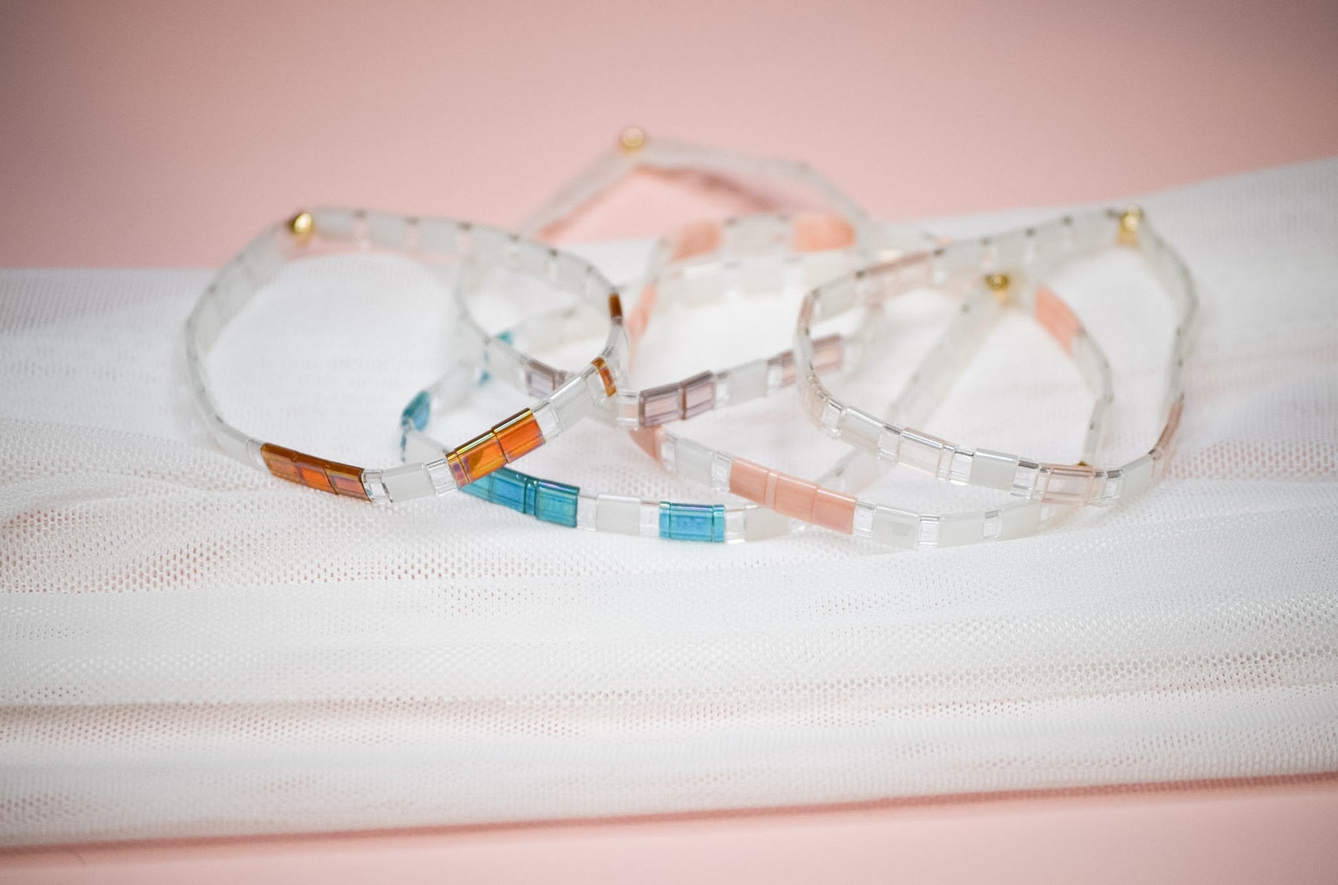 Set of colorful bracelets on a white surface with a pink background