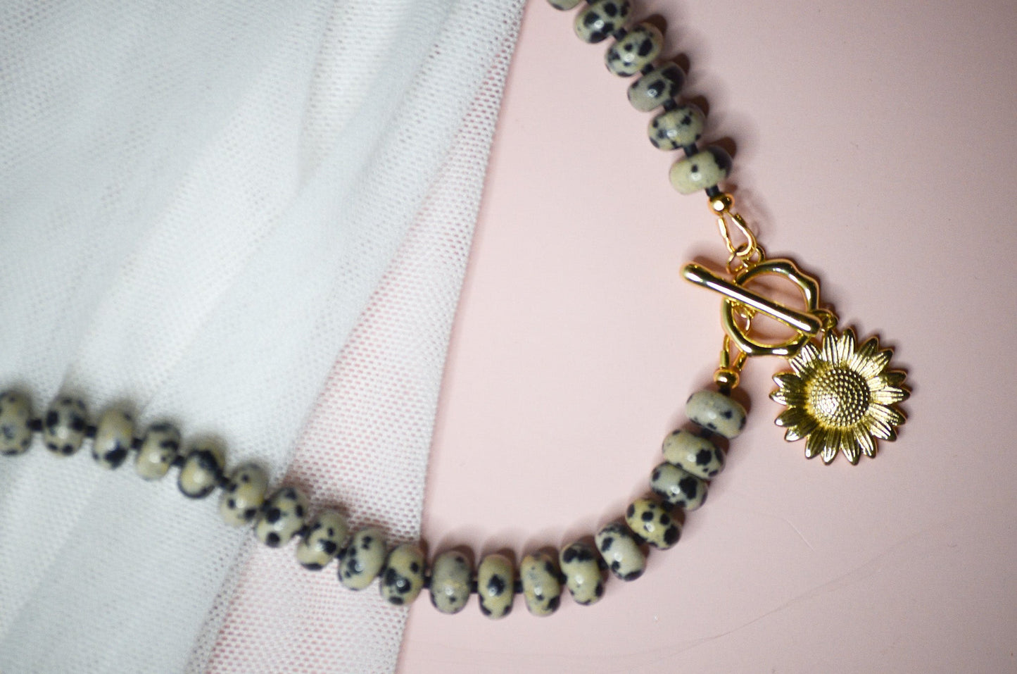 Beaded bracelet with a gold clasp and sunflower charm on a pink and white background