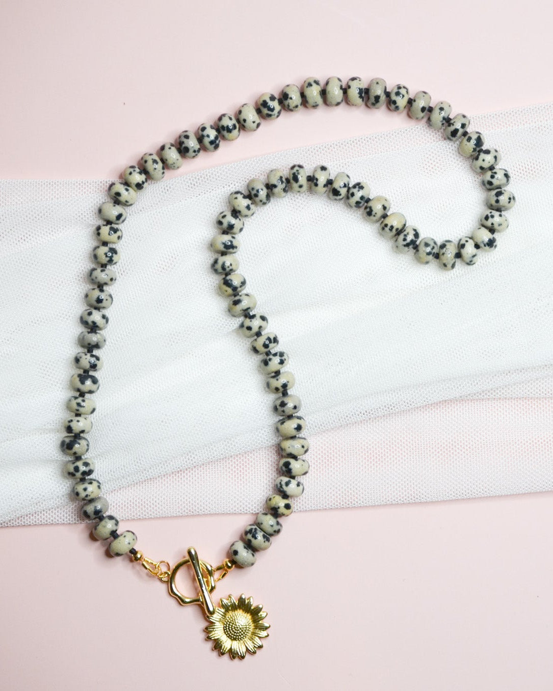 Necklace with sun pendant on a pink and white surface