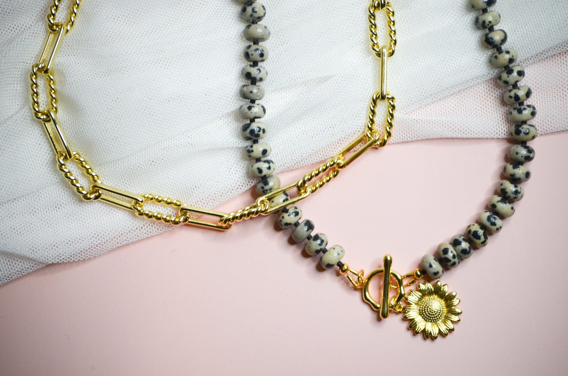 One gold necklace with a  beaded necklace on a light pink background