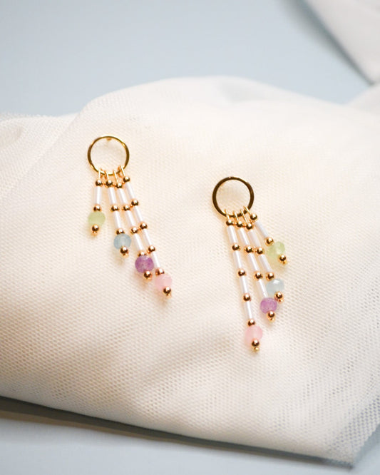 Gold circle earrings with colorful dangle beads on a white fabric surface