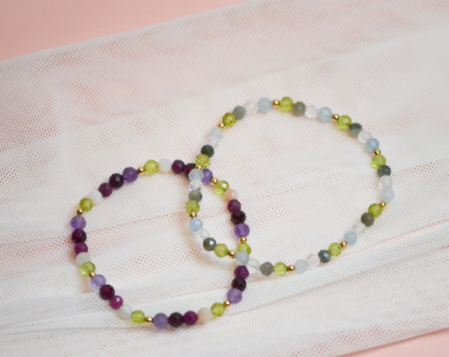 Two beaded birthstone bracelets on a white fabric background