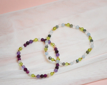 Two beaded birthstone bracelets on a white fabric background