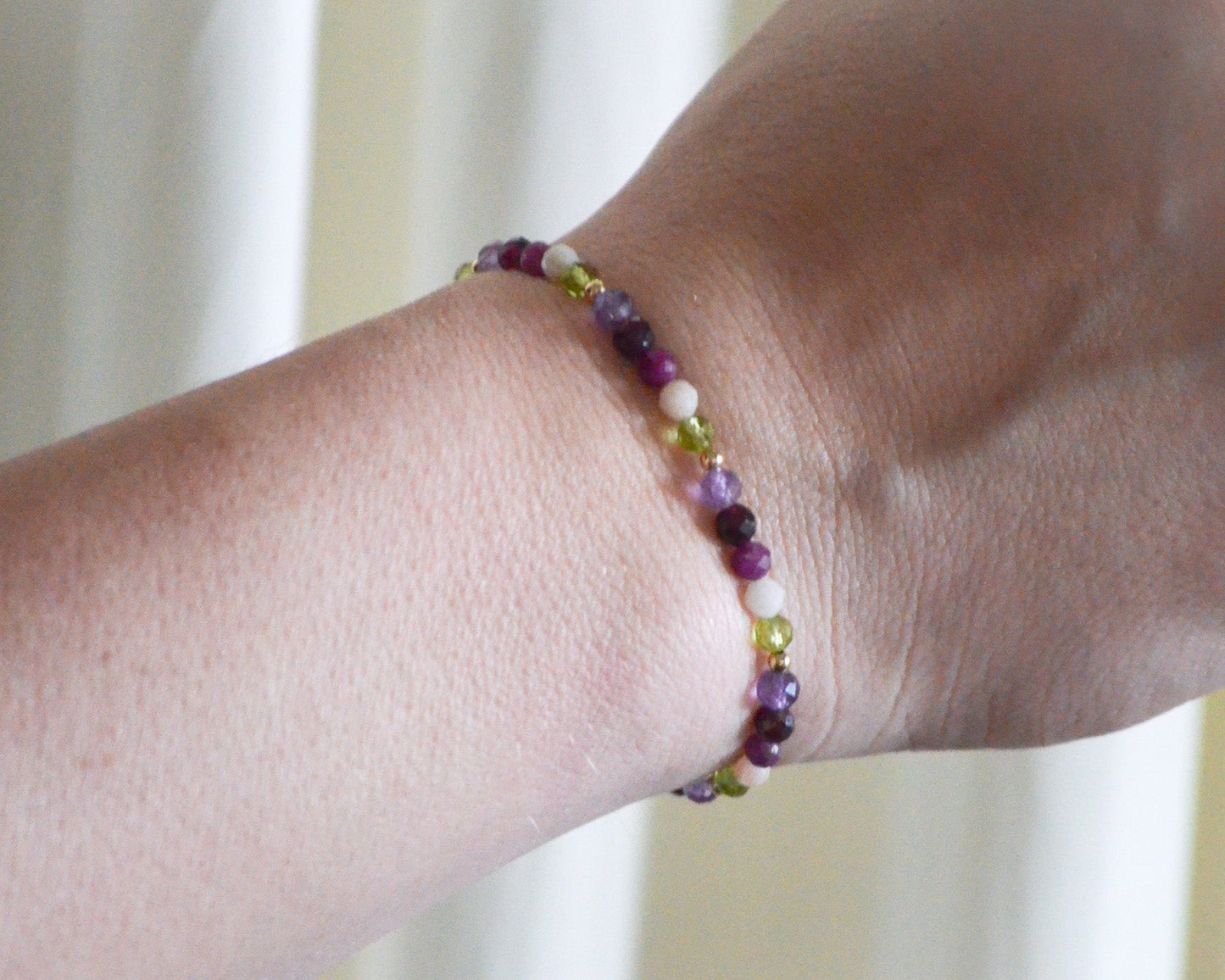 Multicolored beaded birthstone bracelet on a wrist with a blurred background